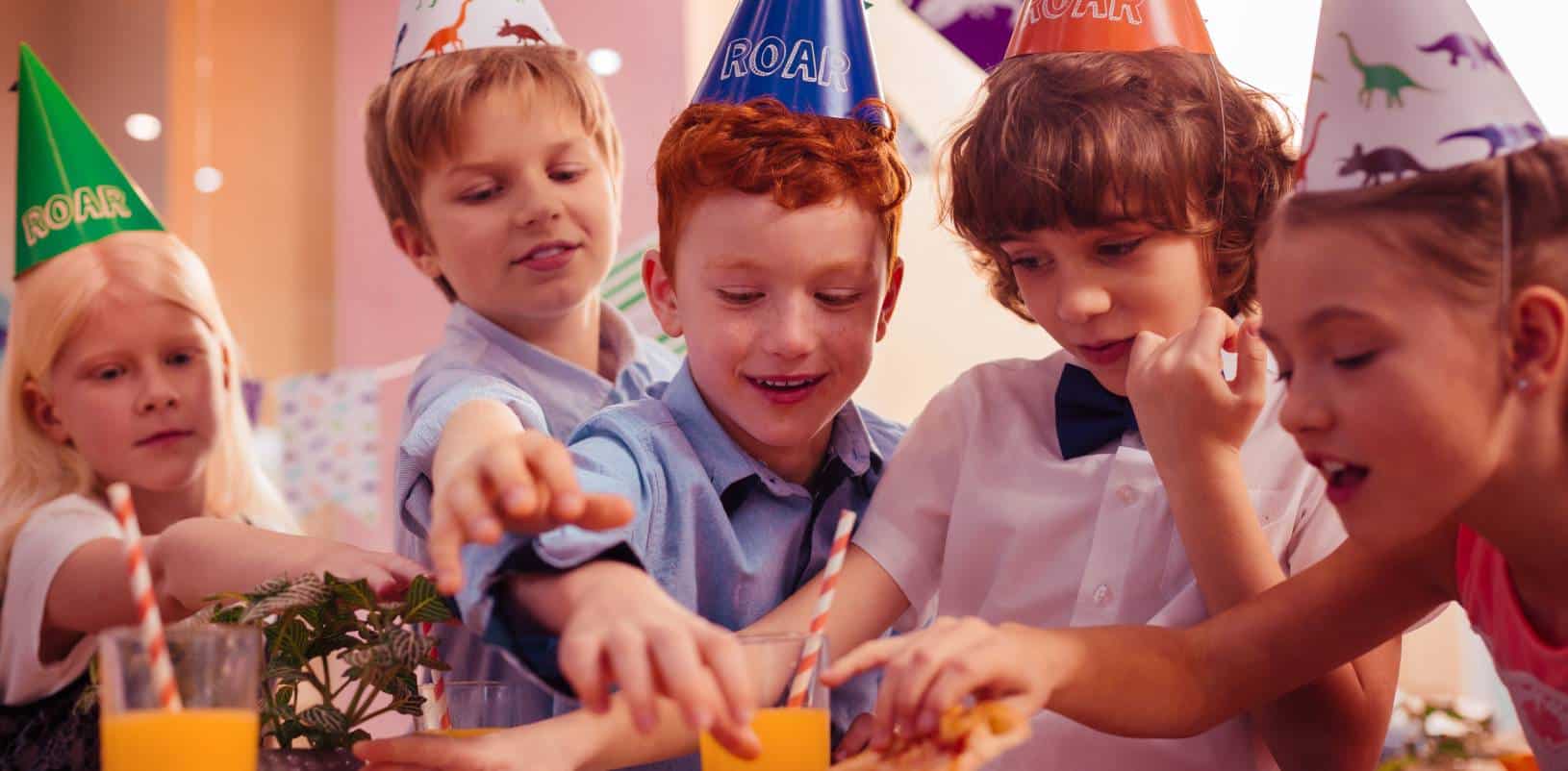 Children in dinosaur party hats enjoy snacks at a science center birthday party for kids and families, STEM fun