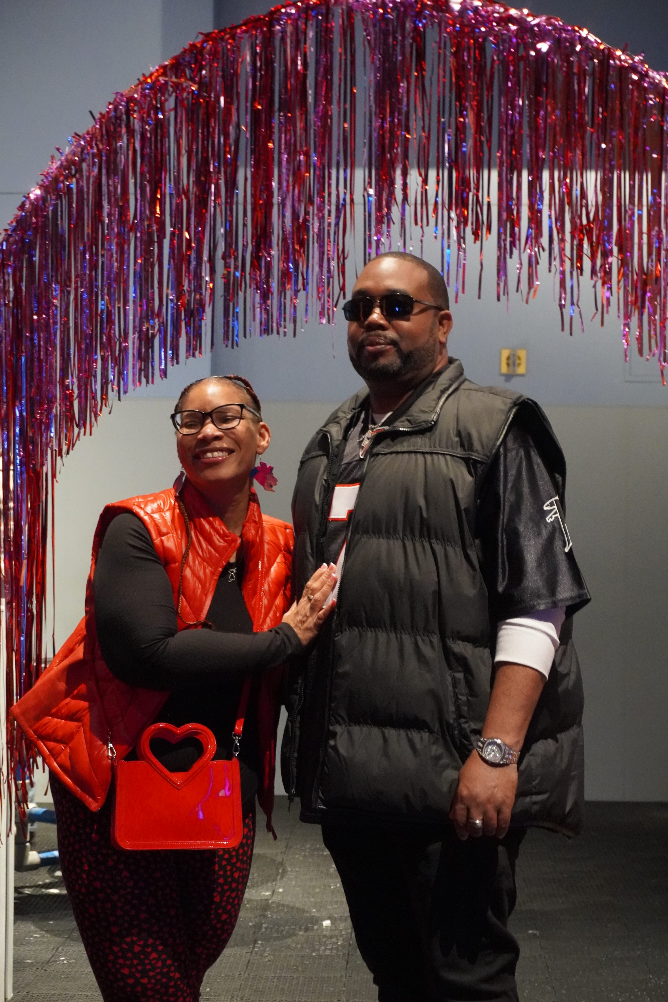A woman and a man smile under a red tinsel arch at a children's science center event.