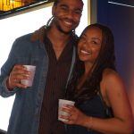 Two adults smiling with drinks at a children's science center exhibit during an evening event.