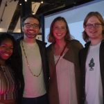 Four adults at a children's science center event, smiling by interactive exhibits.