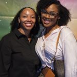 Two visitors smile at the children's science center astronomy exhibit with a galaxy backdrop.