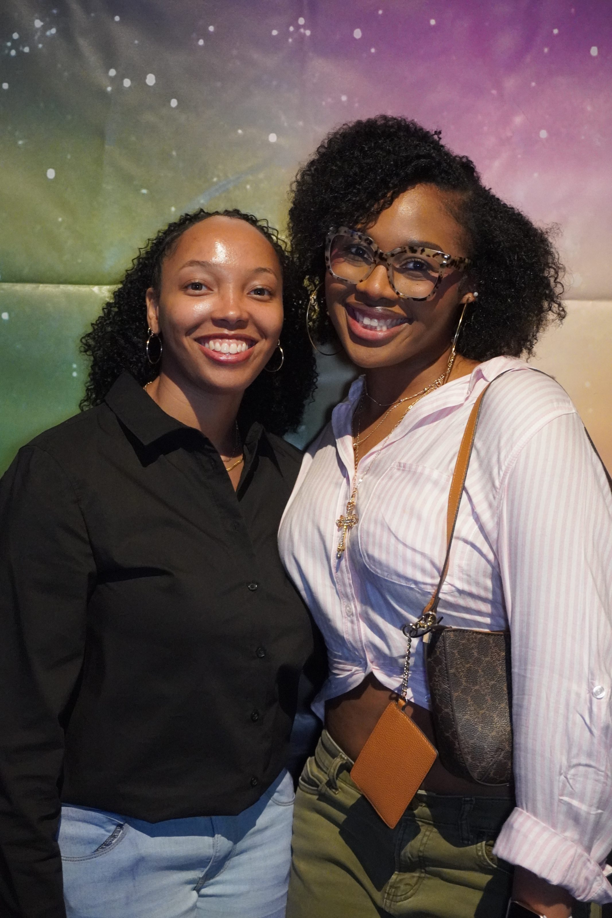 Two visitors smile at the children's science center astronomy exhibit with a galaxy backdrop.