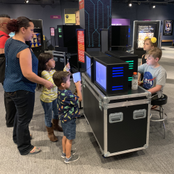 Kids and a parent explore hands-on STEM exhibit with interactive screens at a children's science center